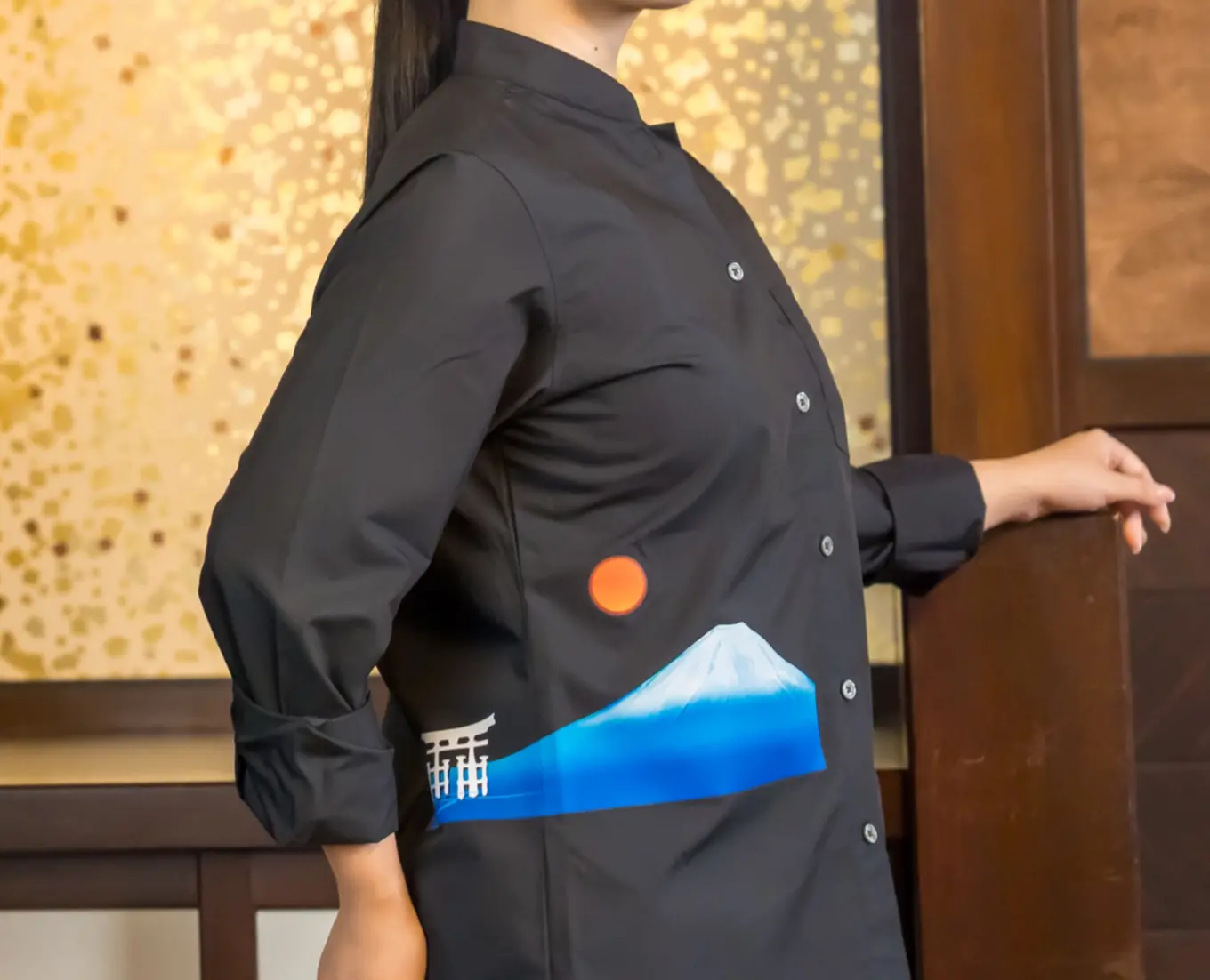 Hospitality staff wearing a black uniform shirt with a Mount Fuji motif, welcoming guests